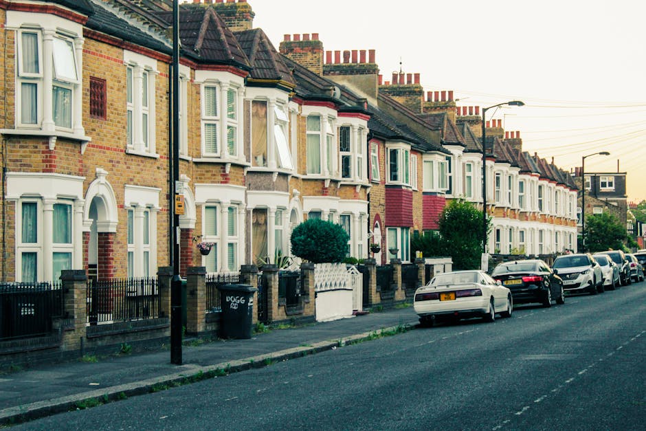 A row of terraced Victorian-style houses with brick facades and white bay windows along a residential street in Battersea, SW11. The pavement in front of the houses is lined with black wrought iron fe