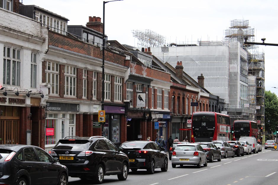 A street scene in Battersea during a home relocation process, with a line of parked cars along the kerbside and a red double-decker bus in travel. The street is lined with traditional brick commercial